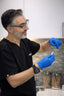 Person in black scrubs and blue gloves holding a syringe in a clinical setting